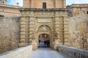 Fototapeta na wymiar Malta, Mdina entrance gate. Tourists cross the footbridge to visit the historic fortified town.