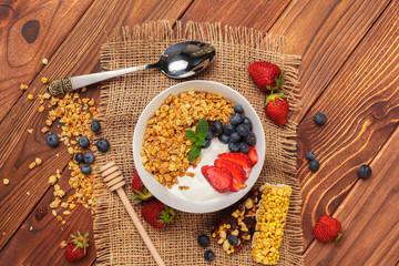 Bowl of homemade granola with yogurt and fresh berries on wooden background