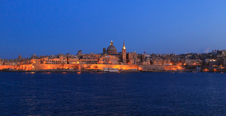 Fototapeta na wymiar Valletta, Malta in the evening. Panoramic view of illuminated historic island and the dome of Carmelite Church and St Paul`s tower.