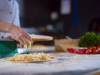 chef sprinkling cheese over fresh pizza dough