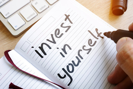 Man is writing invest in yourself in a note.