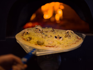 chef putting delicious pizza to brick wood oven