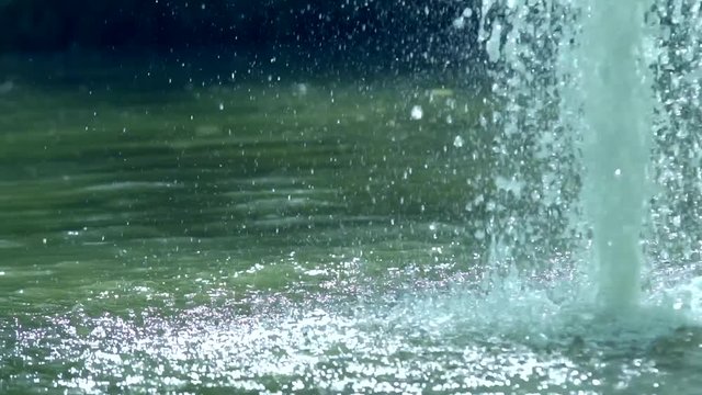 Drops and splashes of water from a powerful jet of a fountain fall downwards scattering in different directions and rising to the top. Slow motion.