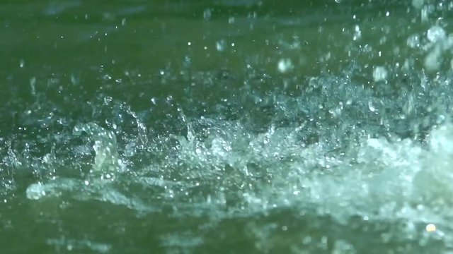 Drops and splashes of water from a powerful jet of a fountain fall downwards scattering in different directions and rising to the top. Slow motion.