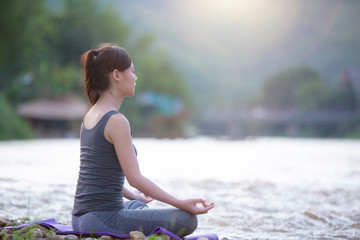 Yoga woman sitting on the river bank in park, Meditation.