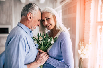 The happy elderly couple standing with flowers