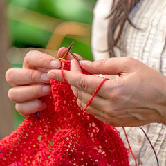 H&auml;nde einer Frau die mit roter Wolle h&auml;kelt / Strickt vor unscharfem Hintergrund