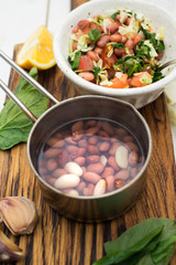 Hot red beans cooked in metal pot for salad with fresh tomatoes, spinach, garlic, lemon, oil, red onion, white cabbage in bowl. Organic farm vegetables. Raw, vegan, vegetarian healthy food concept.