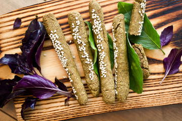 Whole wheat vegan crunchy sticks with sesame seeds and basils leaves on wooden board.