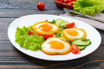 Fried egg in a circle of sweet pepper on a white plate with fresh vegetables on a wooden background. Delicious healthy breakfast. Proper nutrition.