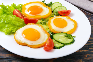 Fried egg in a circle of sweet pepper on a white plate with fresh vegetables on a wooden background. Delicious healthy breakfast. Proper nutrition.