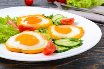 Fried egg in a circle of sweet pepper on a white plate with fresh vegetables on a wooden background. Delicious healthy breakfast. Proper nutrition.