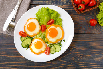 Fried egg in a circle of sweet pepper on a white plate with fresh vegetables on a wooden background. Delicious healthy breakfast. Proper nutrition.