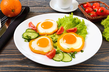 Fried egg in a circle of sweet pepper on a white plate with fresh vegetables, a cup of coffee, fresh oranges on a wooden background. Delicious healthy breakfast. Proper nutrition.