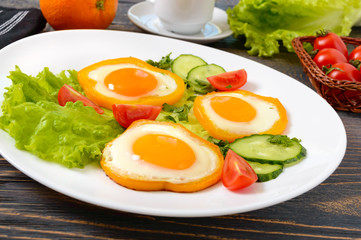 Fried egg in a circle of sweet pepper on a white plate with fresh vegetables, a cup of coffee, fresh oranges on a wooden background. Delicious healthy breakfast. Proper nutrition.
