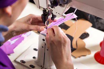 Close-up of a young woman working as a seamstress in a purple unifrome sews genuine leather children's shoes on a sewing machine, top view