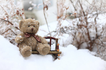 Teddy bear sitting on bench in the winter snow. 