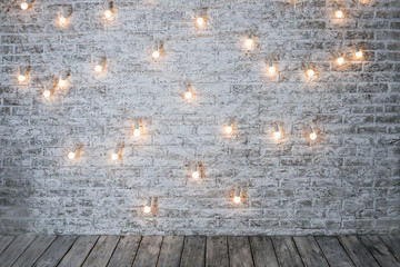 Light bulbs on white brick background with wooden floor. Vintage edison light bulbs garland in loft...