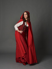 Naklejka premium full length portrait of woman wearing red fantasy costume with cloak, standing pose on grey studio background.