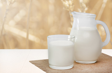 Obraz na płótnie Canvas Jug of milk and glass milk on napkin on white wooden table, blur background
