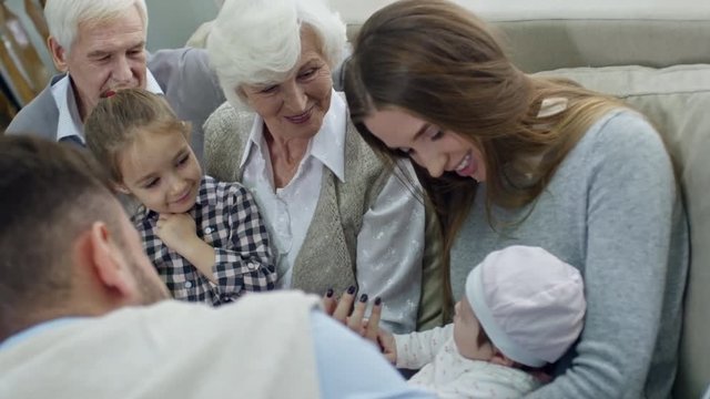 Tilt up of happy grandparents, little girl and young couple cooing over baby