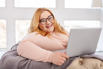 I am happy. Exuberant plump woman smiling while working on her laptop