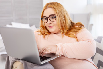 New project. Serious overweight woman wearing glasses and working on her laptop