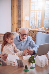 Family relations. Positive aged man sitting together with his granddaughter while spending time together with her