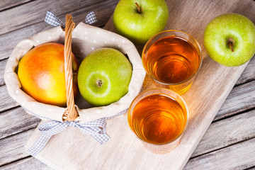 Apple juice in glasses and apples in a wicker basket on wooden table