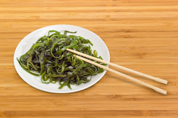 Marinated seaweed salad on white dish with bamboo chopsticks © An-T