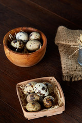 Rustic still life with quail eggs in bucket, box and bowl on a linen napkin over wooden background, selective focus