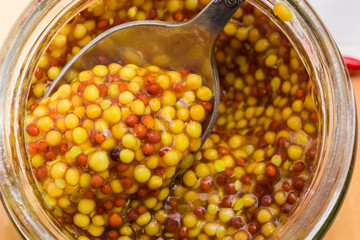 Top view of French mustard on spoon in jar closeup