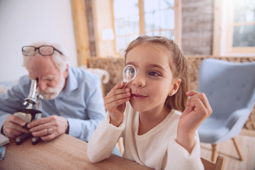 Interesting science. Cute serious girl holding lens while putting it to her eye