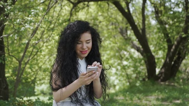 Beautiful brunette chatting with friends by phone in summer garden