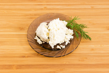 Cottage cheese on glass saucer on bamboo wooden surface