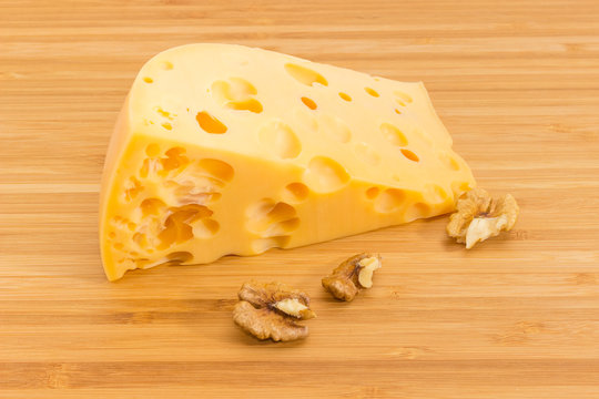 Piece of Swiss cheese and walnuts on bamboo cutting board