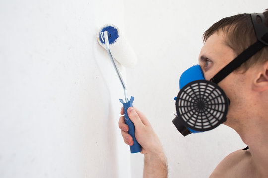 The Worker In A Gas Mask Paints The Roller With A White Wall Paint With A Bad Smell