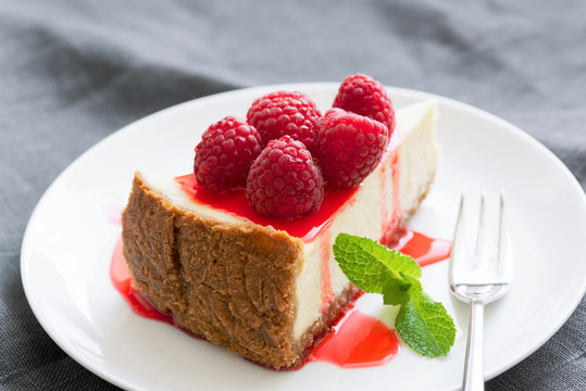 Cheesecake with berry sauce and fresh raspberries on white plate. Selective focus, horizontal composition