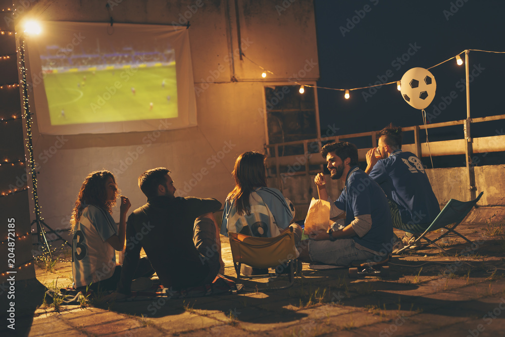 Wall mural Group of friends watching football on a building rooftop - Wall murals