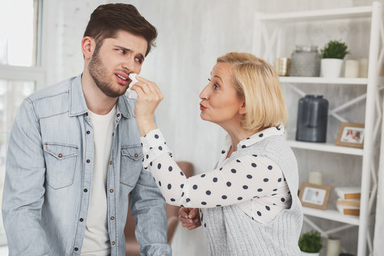 Overcaring mother. Nice aged woman smiling while wiping her sins nose