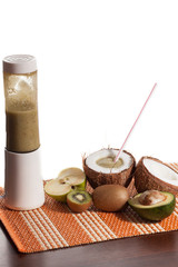 Freshly blended green fruit smoothie in coconut instead of a glass with straw. White background, copy space.