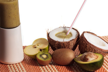 Freshly blended green fruit smoothie in coconut instead of a glass with straw. White background, copy space.