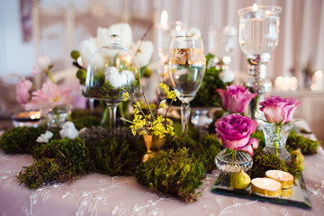 Rustic decoration (forest moss, flowers, candles, glasses and vases). Evening romantic atmosphere.