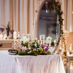 A table for two. Romantic atmosphere in subdued light, lighted candles and rustic decoration (forest moss, flowers, glasses and vases)