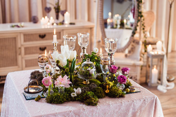 A table for two. Romantic atmosphere in subdued light, lighted candles and rustic decoration (forest moss, flowers, glasses and vases)