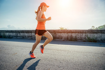 An asian woman athletic is jogging on the concrete road, she is warming her body and tideten her tying her shoes tightly fitting before workout.