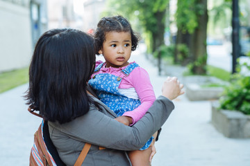 Ecuadorian mother carry her dark skinned toddler baby girl on city street. Side view. No to...