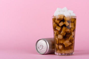 Drinking glass of of lump sugar cubes and soft cola drink with aluminum can on pink pastel background. Unhealthly diet with sweet sugary soft drinks concept.