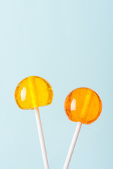 Two big bright tasty lollipops on white sticks blue pastel background vertical with copy space