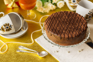 Festive table with chocolate cake on plate, tea set, spoons